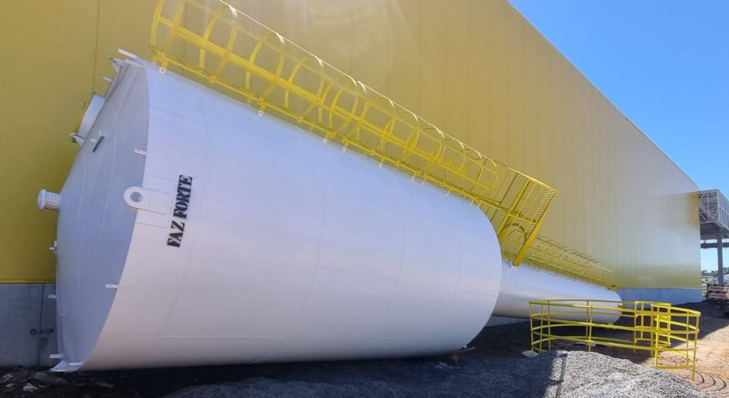 Caixa d'agua Faz Forte de grande porte deitada no chão para manutenção preventiva com container amarelo e céu ao fundo